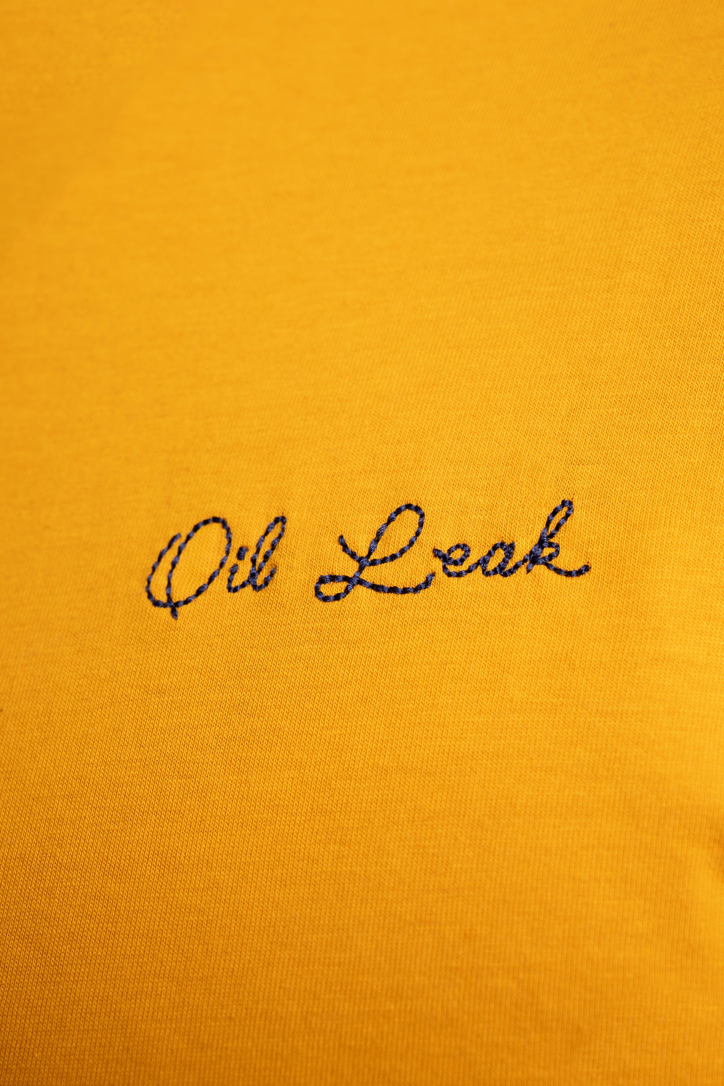 Text 'Oil Leak' embroidered on a mustard yellow background