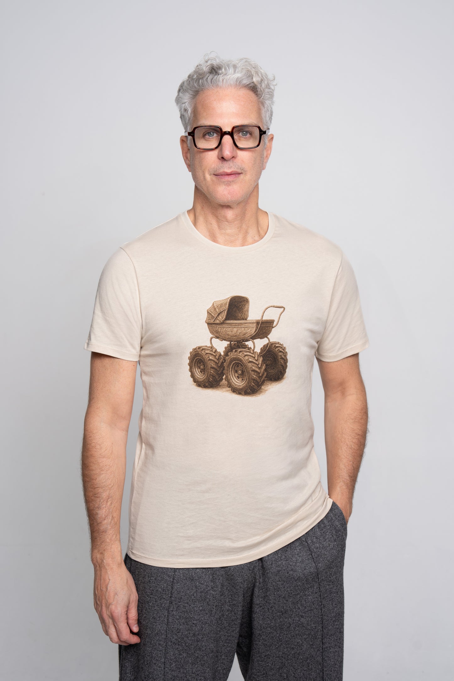 Man wearing a beige t-shirt with a graphic design of a baby carriage on tractor wheels on a plain background